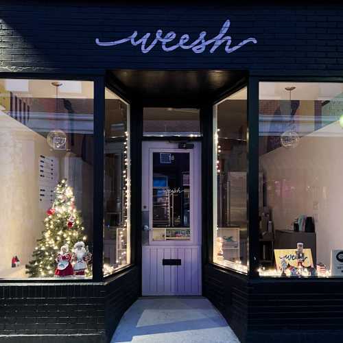 A storefront with the name "weesh," featuring a small Christmas tree and festive lights in the window.