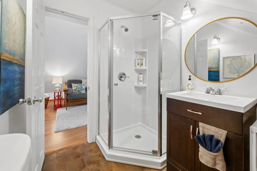 A modern bathroom featuring a glass shower, vanity with sink, and a cozy living area visible in the background.