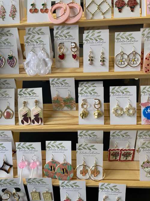 A display of various colorful earrings on cards, featuring different shapes and designs, arranged on wooden shelves.