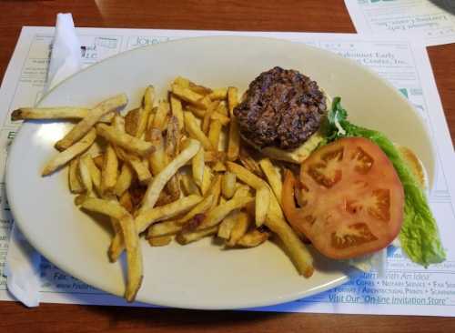 A plate with a hamburger patty on a bun, lettuce, tomato, and a side of golden French fries.