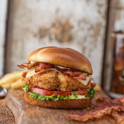 A delicious chicken sandwich with bacon, lettuce, tomato, and cheese on a toasted bun, served with fries.