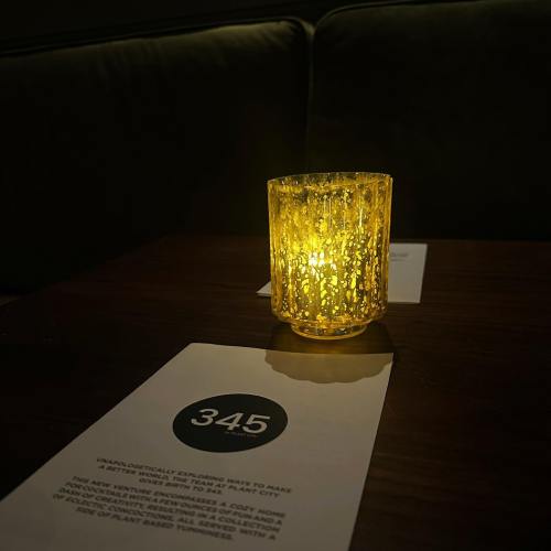 A glowing yellow candle holder on a table with a menu featuring the number 345. Soft lighting creates a cozy atmosphere.