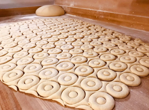 A wooden surface covered with neatly arranged dough circles, with a larger ball of dough in the background.
