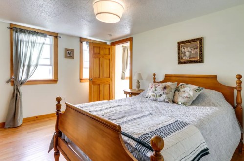 Cozy bedroom with a wooden bed, floral pillows, and natural light from windows, featuring a warm color palette.