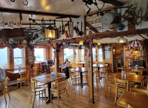 Cozy restaurant interior with wooden tables, chairs, and vintage decor, featuring large windows and a warm atmosphere.