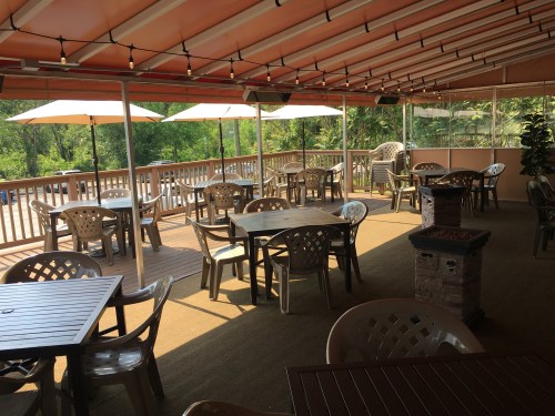A spacious outdoor dining area with tables, chairs, and umbrellas, surrounded by greenery and natural light.