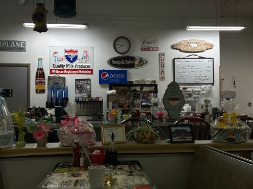 A cozy diner interior featuring a menu board, vintage signs, and decorative baskets on a counter.