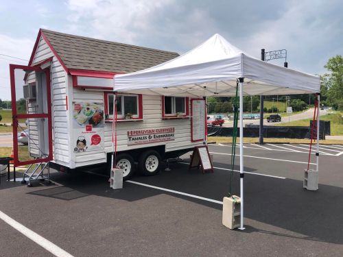 A food truck with a white and red exterior, serving Peruvian cuisine, parked under a canopy on a sunny day.