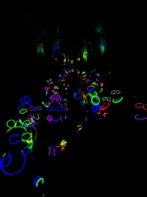 A crowd of people wearing glowing neon accessories in a dark setting, creating a vibrant, colorful atmosphere.