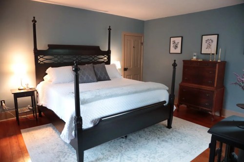 A cozy bedroom featuring a black four-poster bed, wooden dresser, and soft blue walls.