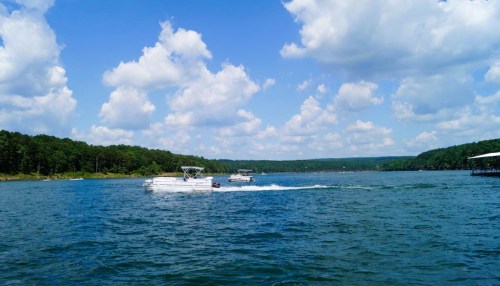 A scenic view of a lake with boats cruising under a blue sky filled with fluffy white clouds.