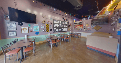 A colorful restaurant interior with tables, wall art, and a large sign that says "Wake Me Up When I'm Famous."