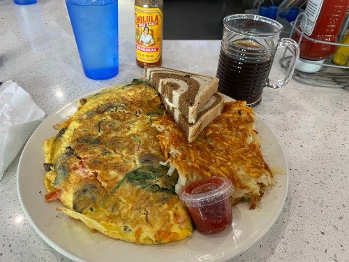 A plate with a vegetable omelette, hash browns, toast, a small cup of salsa, and a drink on a table.