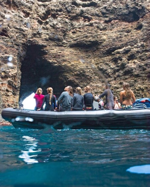 A group of people on a boat near a rocky cave entrance, surrounded by water.