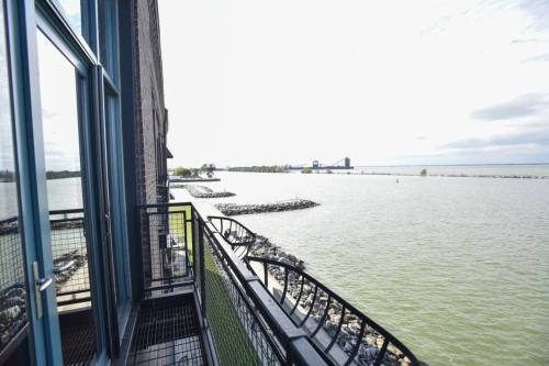 View from a balcony overlooking a calm lake with rocky shorelines and distant industrial structures.