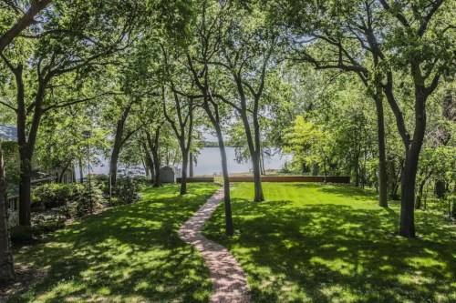 A serene landscape featuring a grassy area bordered by trees, leading to a calm lake in the background.