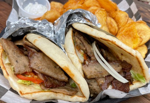 Two pita wraps filled with sliced meat, lettuce, and tomatoes, served with a side of crispy potato chips.