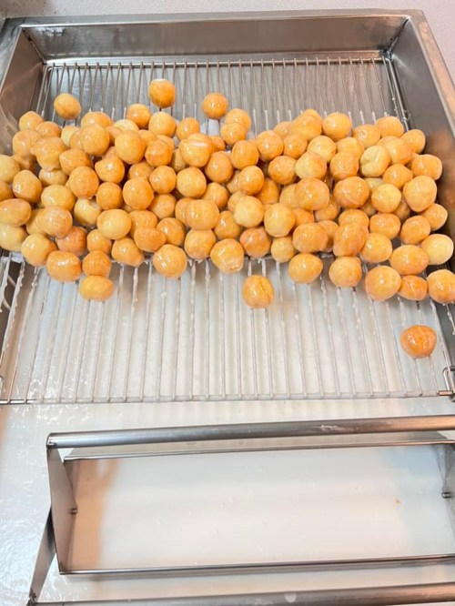 A metal tray filled with numerous golden, round dough balls, glistening with a light glaze.