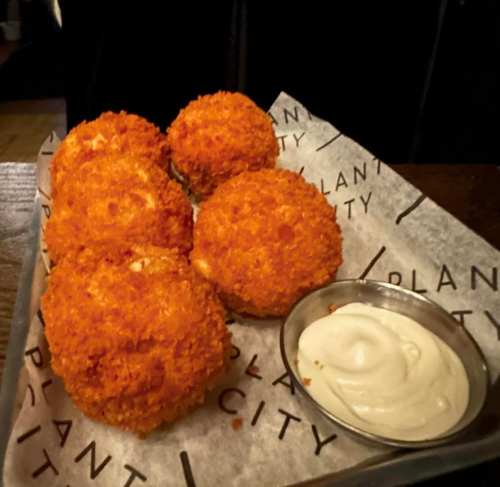 Five golden, crispy croquettes on a tray with a small bowl of creamy dipping sauce.