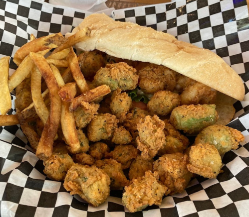 A basket of fried okra and French fries, with a sandwich on top, served in a checkered paper liner.