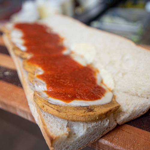 A slice of bread topped with sauce and layers of sliced ingredients, ready for assembly.
