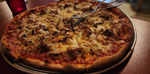 A large pizza topped with sausage, mushrooms, and cheese, served on a round tray with tongs.