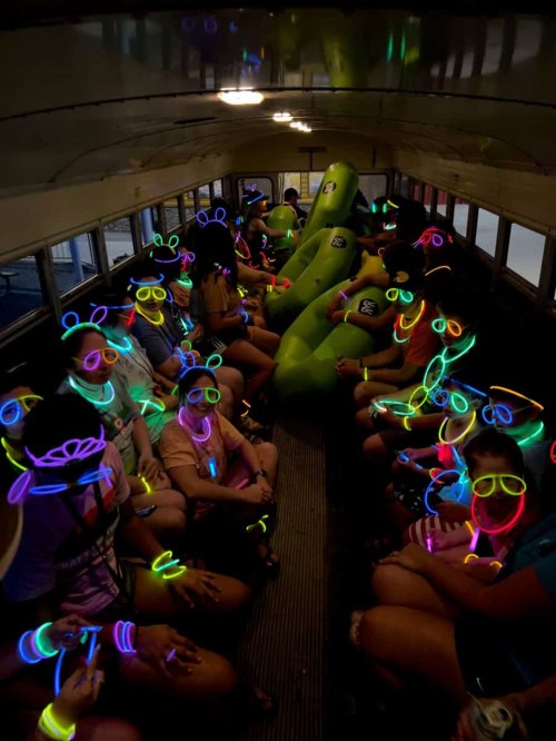 A group of people inside a bus wearing colorful glow sticks and accessories, creating a vibrant, festive atmosphere.