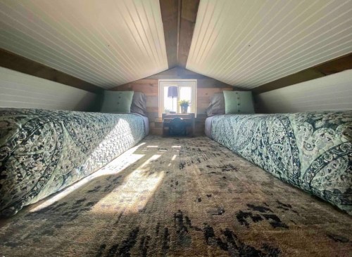 Cozy attic room with two beds, decorative pillows, and a window letting in natural light.