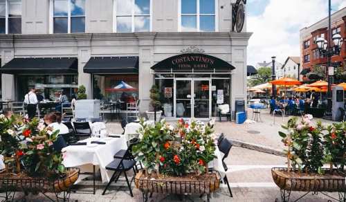 Outdoor dining area with tables, flowers, and umbrellas at Costantino's restaurant on a sunny day.