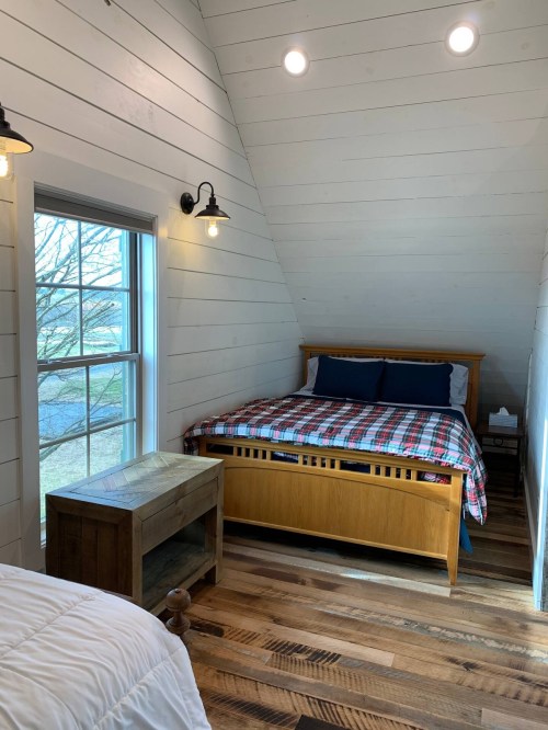 Cozy bedroom with sloped ceiling, wooden bed, plaid bedding, and a window letting in natural light.