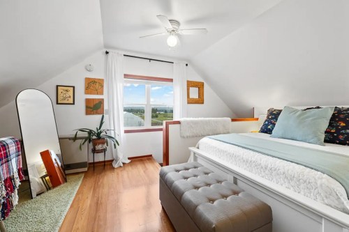 Cozy attic bedroom with a bed, mirror, and large window, featuring light decor and wooden flooring.