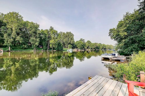 A serene river scene with lush trees, a wooden dock, and calm water reflecting the sky.