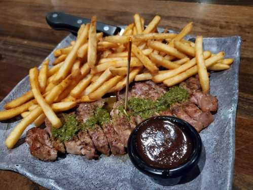 A plate of sliced steak drizzled with sauce, accompanied by a side of crispy French fries.