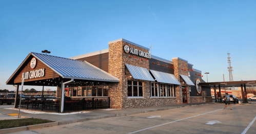 Exterior of a modern chicken restaurant with a brick facade and outdoor seating, under a clear blue sky.
