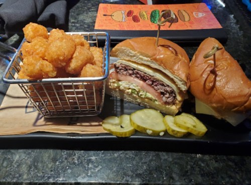 A plate with two sandwiches and a basket of tater tots, accompanied by pickles on the side.