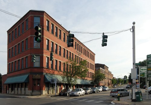 A brick building at a street corner with traffic lights and parked cars, under a clear sky.