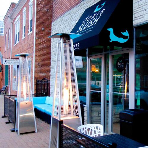Exterior of a café named "Doxie Slush," featuring outdoor seating and patio heaters on a brick street.