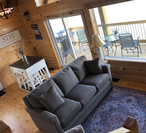 Cozy wooden interior featuring a gray sofa, dining table, and large windows with a view of a deck.