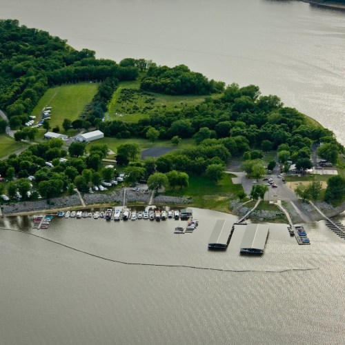 Aerial view of a marina with boats, surrounded by lush greenery and a calm body of water.