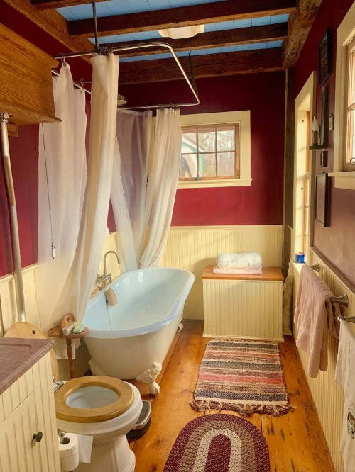 Cozy bathroom featuring a freestanding tub, wooden accents, and warm red walls, with natural light from a window.