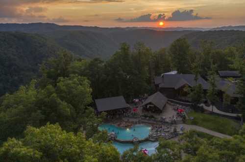 A scenic view of a sunset over mountains, featuring a pool and lodge surrounded by lush trees.