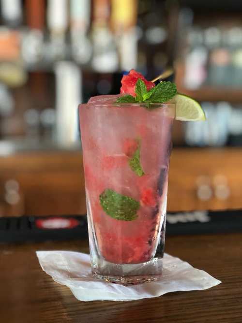 A refreshing cocktail with mint leaves and lime, served in a tall glass filled with ice and watermelon chunks.