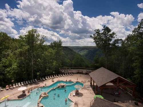 A scenic view of a pool surrounded by trees and mountains, with people enjoying the water under a cloudy sky.