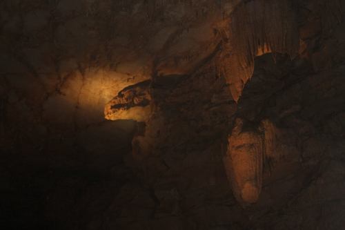 Stalactites and stalagmites illuminated in a dark cave, showcasing natural rock formations.