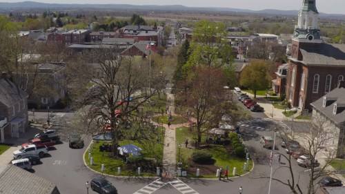 Aerial view of a small town square with trees, a park, and buildings in the background on a sunny day.