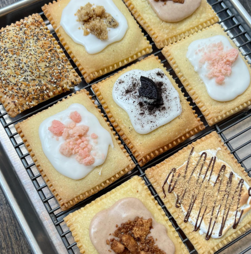 A tray of nine frosted pastries with various toppings, including sprinkles, cookies, and chocolate drizzles.