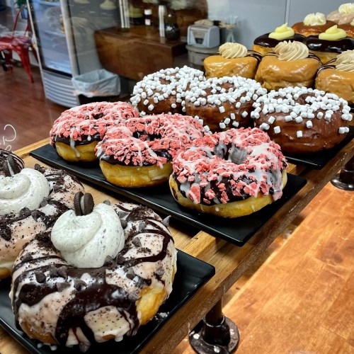 A display of colorful donuts with various toppings, including chocolate, sprinkles, and cream, on black plates.