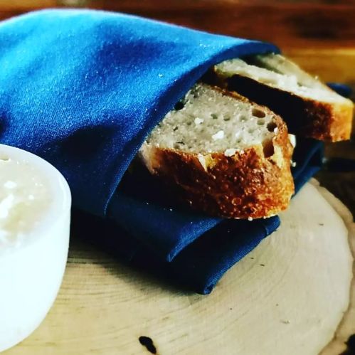Sliced bread peeking out of a blue napkin, next to a small bowl of creamy spread on a wooden surface.