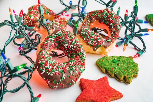 Colorful Christmas donuts with sprinkles, surrounded by festive lights and holiday-shaped cookies.