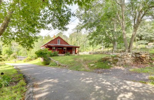 A red house surrounded by trees and greenery, with a gravel driveway leading up to it.